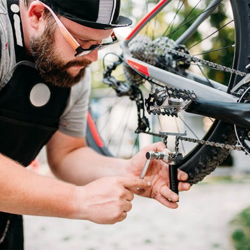 bicycle-mechanic-in-apron-adjusts-bike-chain-PKRWA26.jpg