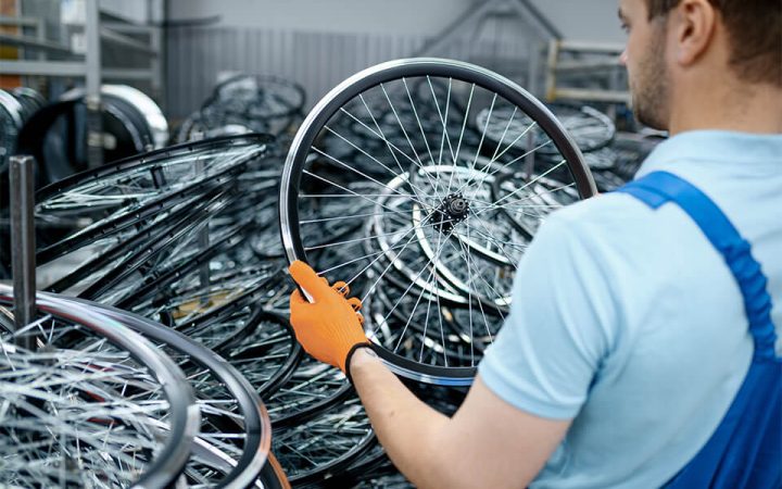 mechanic-in-uniform-holds-bicycle-wheel-on-factory-3NYHRNN.jpg